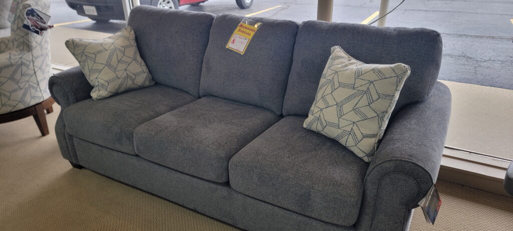Charcoal gray Decor-Rest sofa with rolled arms and cube-pattern accent pillows, on showroom floor.