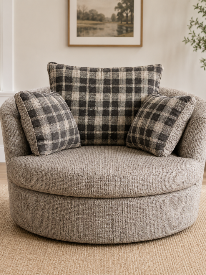 Oversized round swivel accent chair with textured gray upholstery and plaid accent pillows in a warm neutral living room