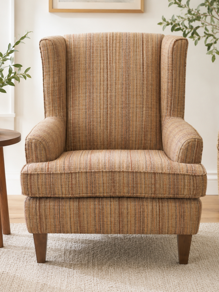 Textured upholstered wingback accent chair with warm striped fabric and wooden legs in a bright modern living room setting.