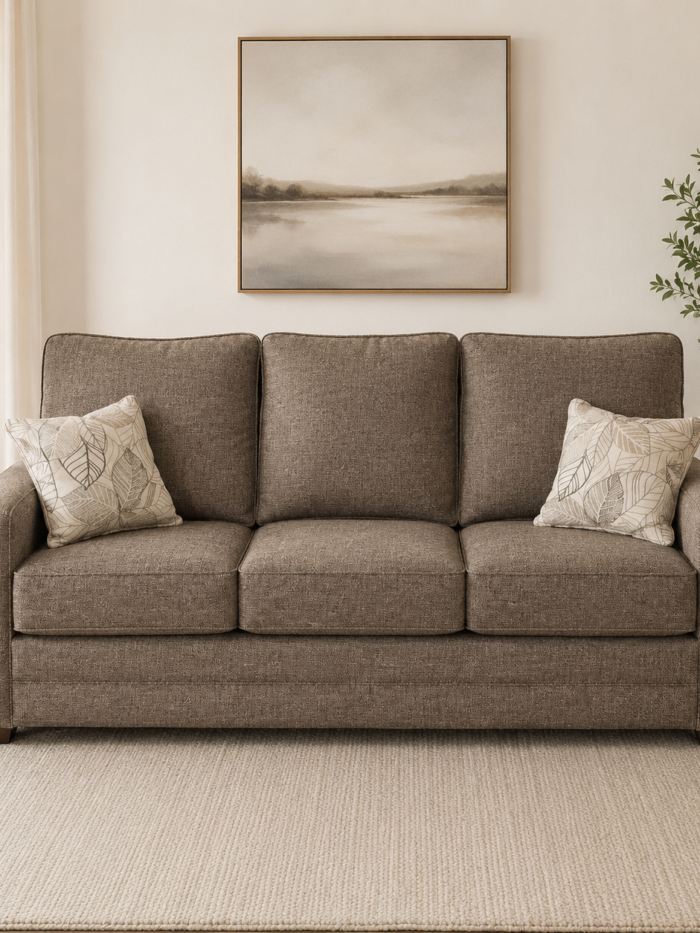 Brown upholstered three-cushion sofa with accent pillows displayed in a bright neutral living room setting.