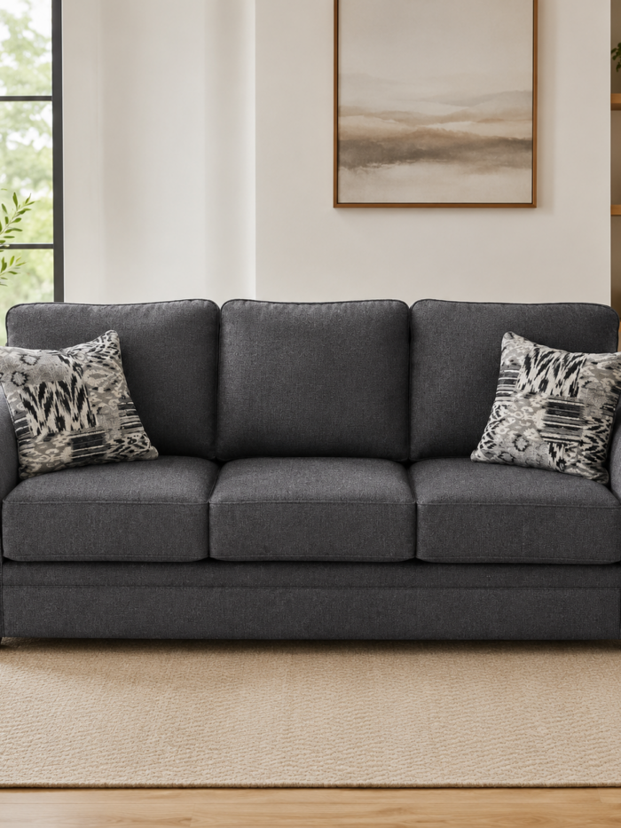 Charcoal gray three-cushion upholstered sofa with patterned accent pillows in a bright modern living room.